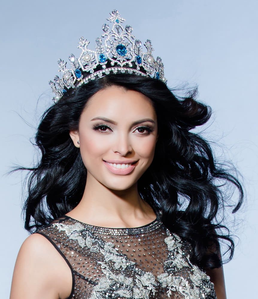 Portrait of a woman wearing a sparkling crown and a sequined dress, smiling against a light background.