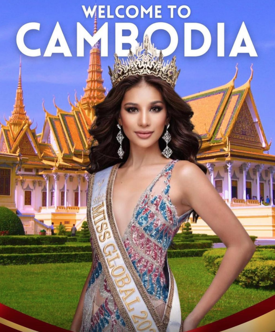 A woman wearing a "miss global 2019" sash and crown stands before a backdrop of the royal palace in cambodia.