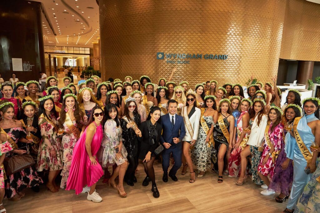 Group photo of diverse people in colorful outfits at a hotel lobby event, posing joyfully around a central figure.