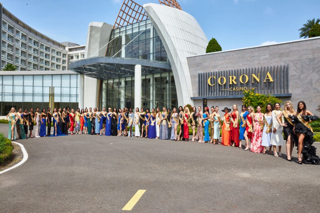 Group of women in various traditional dresses standing outside the corona casino building under a clear sky.