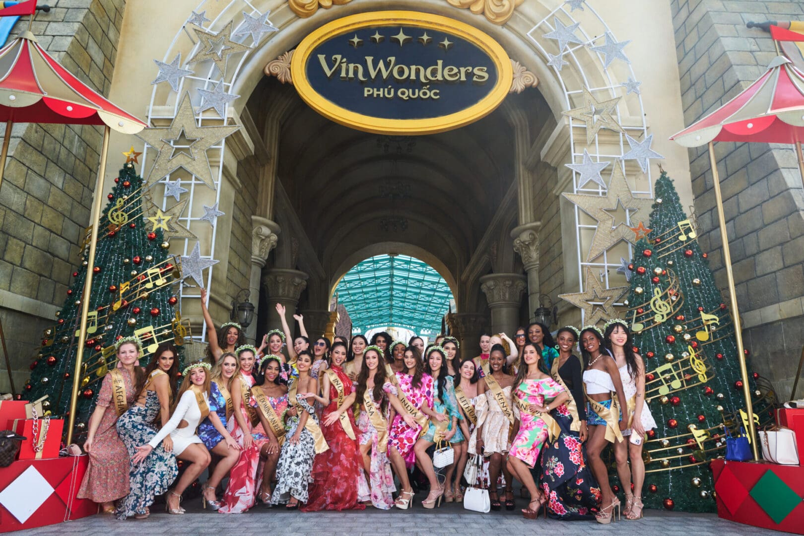 Group of women in diverse formal attire posing in front of vinwonders phu quoc entrance decorated for christmas.